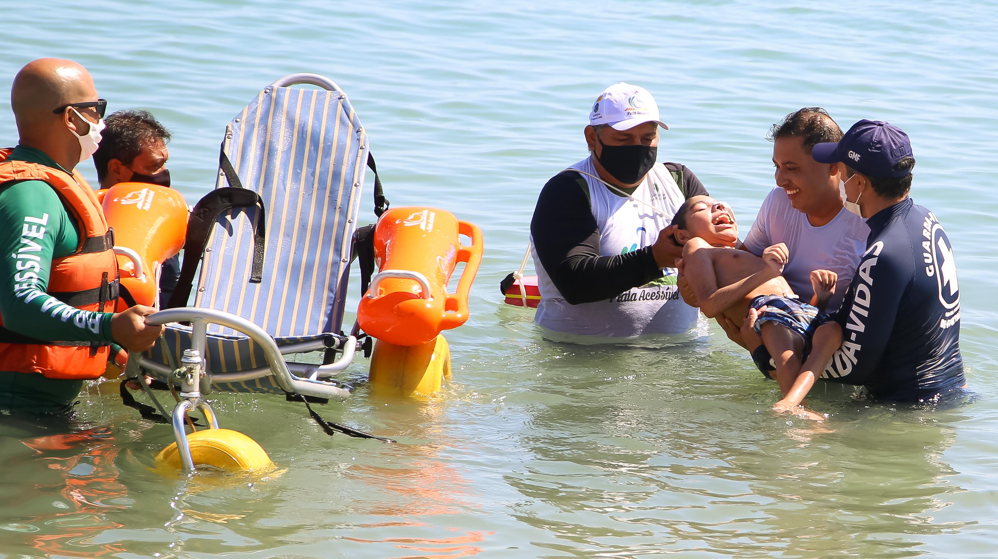 cuidadores do programa praia acessível dão banho de mar em um jovem